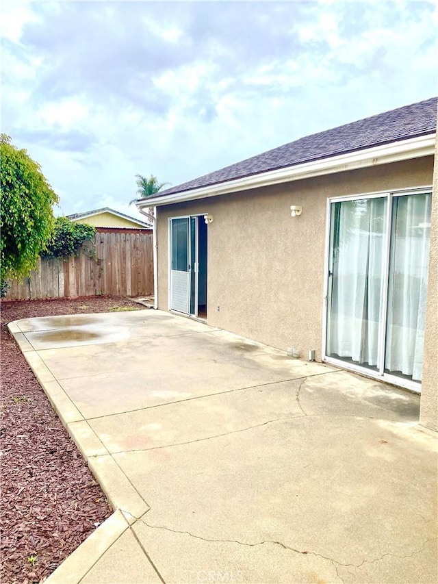 rear view of house featuring stucco siding, a patio, a shingled roof, and fence