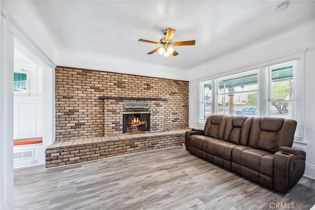 401 Cibola St, Needles, CA 92363 - living room with a ceiling fan, a brick fireplace, wood finished floors, brick wall, and healthy amount of natural light