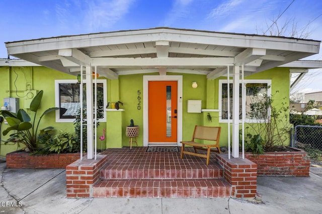 doorway to property featuring stucco siding, a porch, and fence