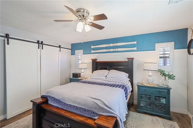 33971 Lily Rd, Yucaipa, CA 92399 - bedroom with a barn door, wainscoting, wood finished floors, a ceiling fan, and multiple windows
