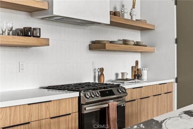 kitchen with open shelves, stainless steel range with gas stovetop, light countertops, exhaust hood, and tasteful backsplash