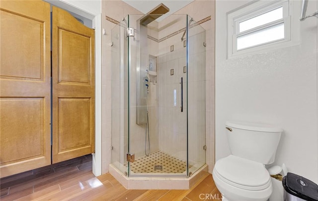 bathroom with toilet, wood finished floors, and a stall shower