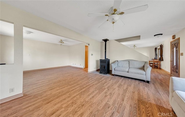 unfurnished living room with light wood-style flooring, a ceiling fan, baseboards, and a wood stove