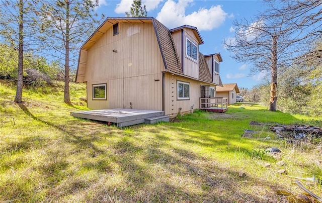 rear view of property with a gambrel roof, a lawn, a deck, and a shingled roof