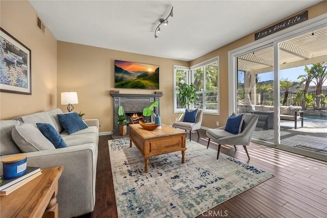 living area featuring visible vents, hardwood / wood-style flooring, a warm lit fireplace, rail lighting, and baseboards