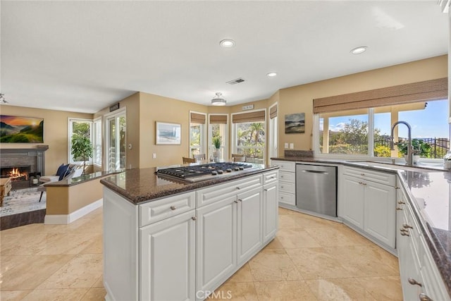 kitchen featuring a center island, a lit fireplace, white cabinets, stainless steel appliances, and a sink