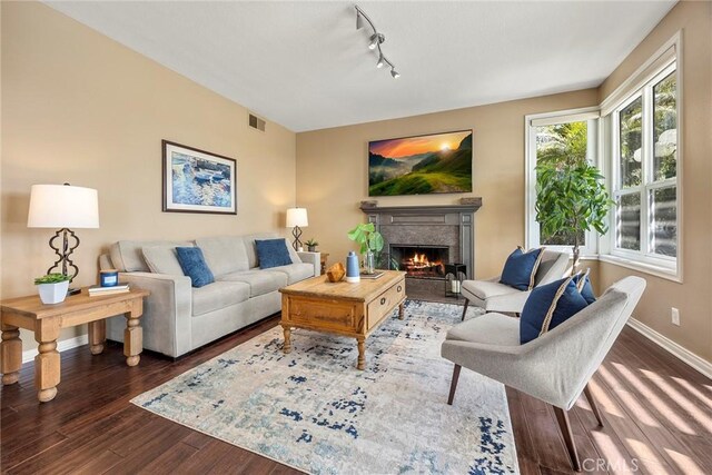 living room featuring visible vents, a warm lit fireplace, wood finished floors, rail lighting, and baseboards