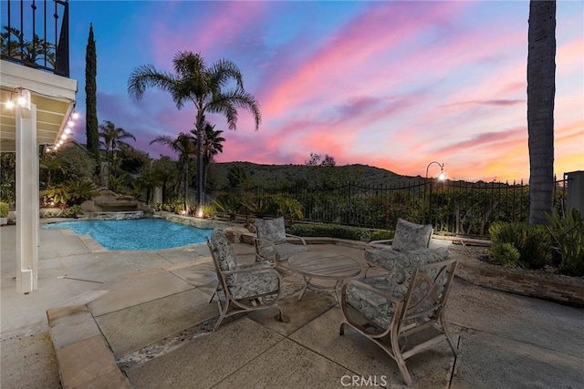 pool at dusk featuring a fenced in pool and a patio