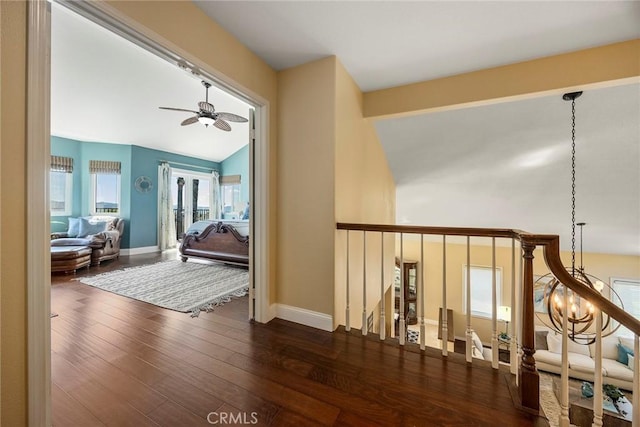 hallway featuring vaulted ceiling, wood finished floors, baseboards, and a chandelier