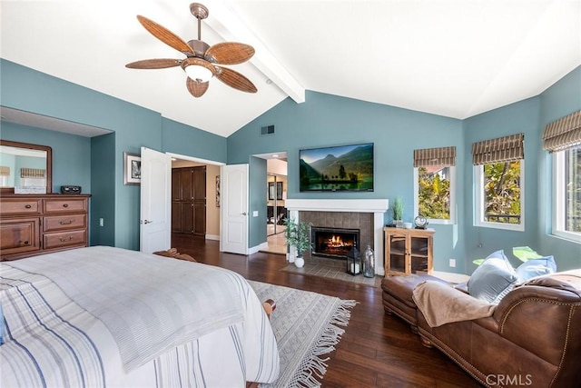 bedroom featuring wood finished floors, baseboards, visible vents, lofted ceiling with beams, and a tile fireplace