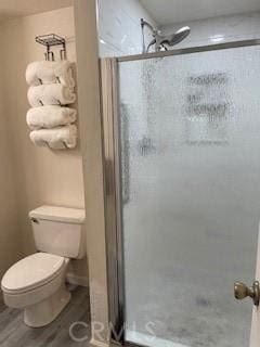 bathroom with toilet, wood finished floors, and a stall shower