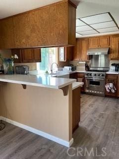 kitchen featuring under cabinet range hood, light countertops, a peninsula, a kitchen breakfast bar, and high end range