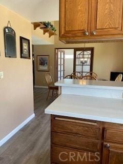 kitchen featuring baseboards, dark wood-style flooring, brown cabinetry, and light countertops