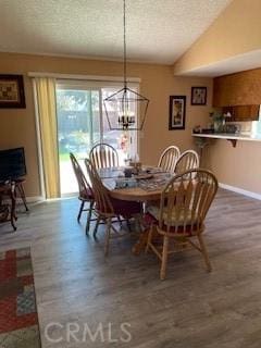 dining room featuring lofted ceiling, a textured ceiling, wood finished floors, an inviting chandelier, and baseboards