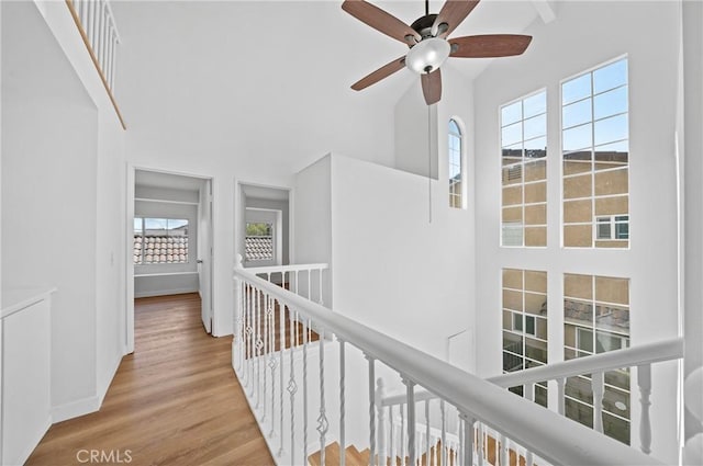 hallway featuring a high ceiling, an upstairs landing, wood finished floors, and a wealth of natural light