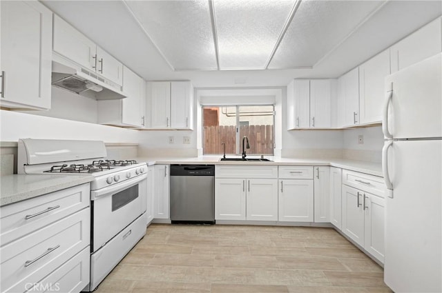 kitchen featuring a sink, under cabinet range hood, white appliances, white cabinets, and light countertops