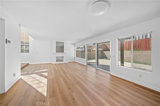 unfurnished living room featuring wood finished floors, a fireplace, baseboards, and a healthy amount of sunlight