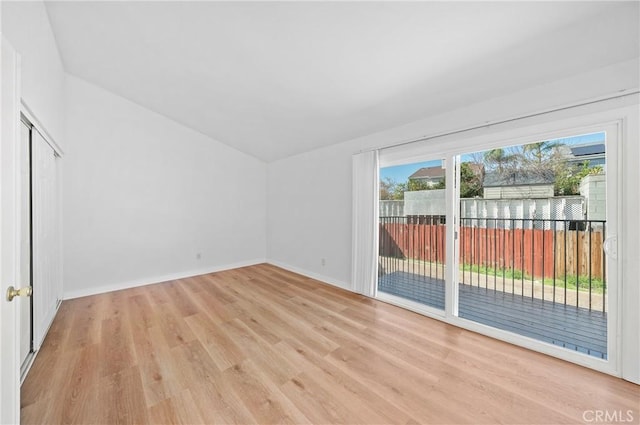 spare room featuring light wood-style flooring, baseboards, and vaulted ceiling