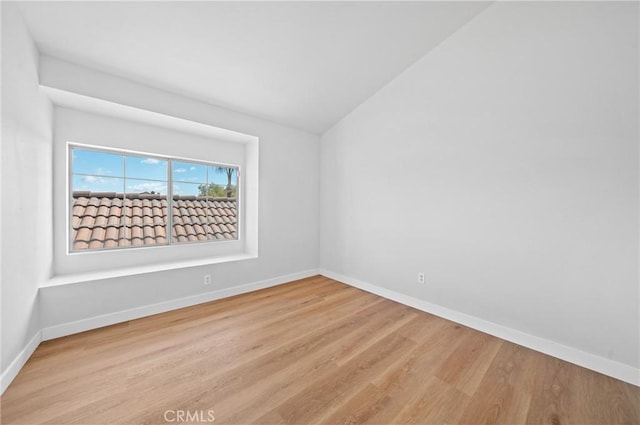 spare room featuring lofted ceiling, baseboards, and wood finished floors