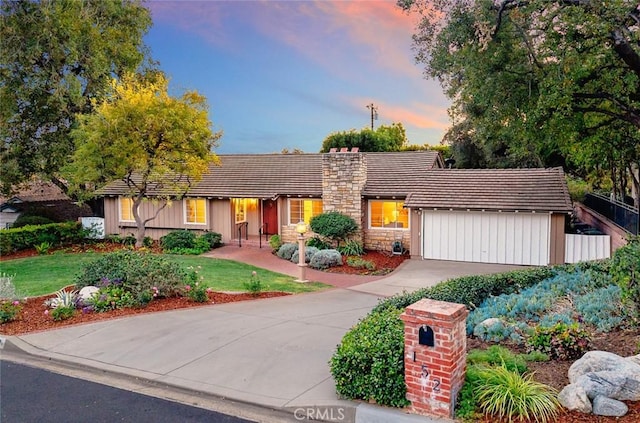 view of front of property with a tile roof, a yard, concrete driveway, an attached garage, and a chimney