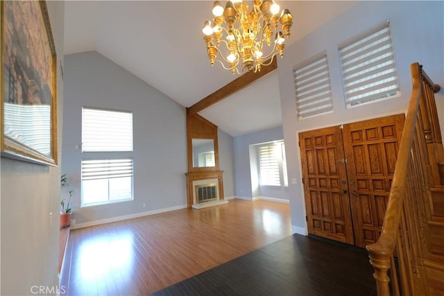 foyer entrance with wood finished floors, a notable chandelier, a healthy amount of sunlight, and high vaulted ceiling