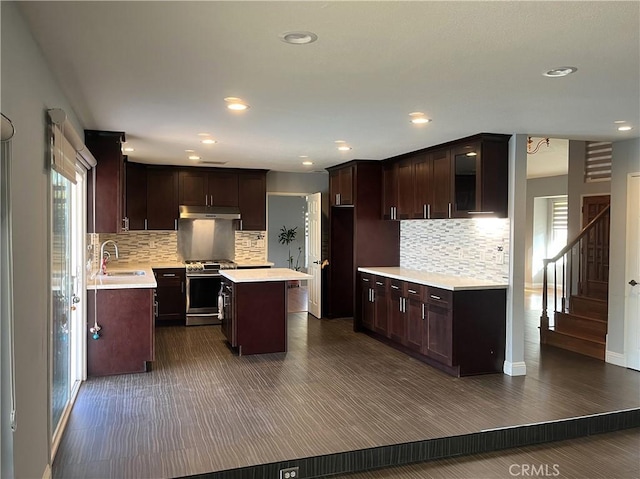 kitchen with a center island, stainless steel range with gas cooktop, under cabinet range hood, light countertops, and a sink