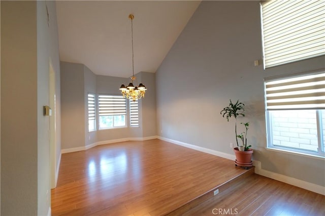 unfurnished room with baseboards, a notable chandelier, wood finished floors, and high vaulted ceiling