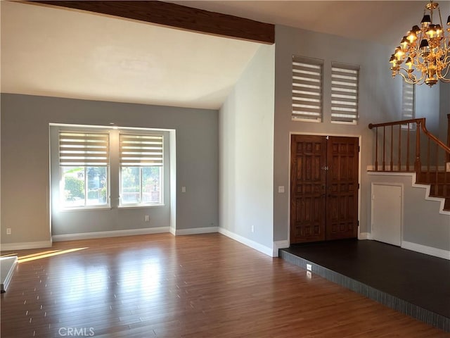 unfurnished living room with baseboards, stairs, an inviting chandelier, and wood finished floors