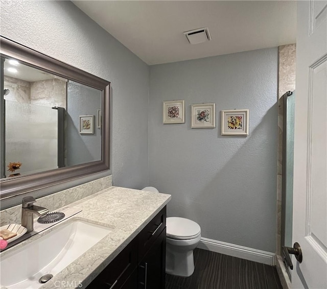 bathroom with vanity, baseboards, visible vents, a shower, and toilet