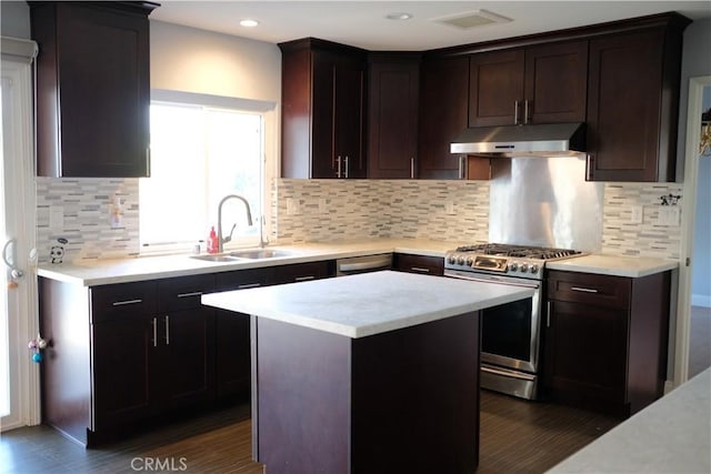 kitchen with gas stove, a sink, dark brown cabinets, under cabinet range hood, and backsplash