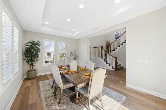 dining room featuring a raised ceiling, recessed lighting, light wood finished floors, baseboards, and stairs