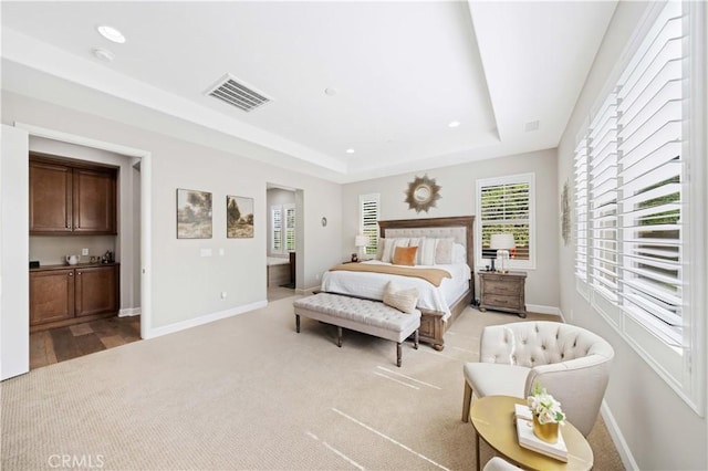 carpeted bedroom with visible vents, a raised ceiling, and baseboards