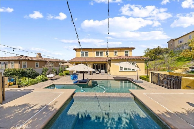 back of property with fence, a patio area, an outdoor pool, and stucco siding