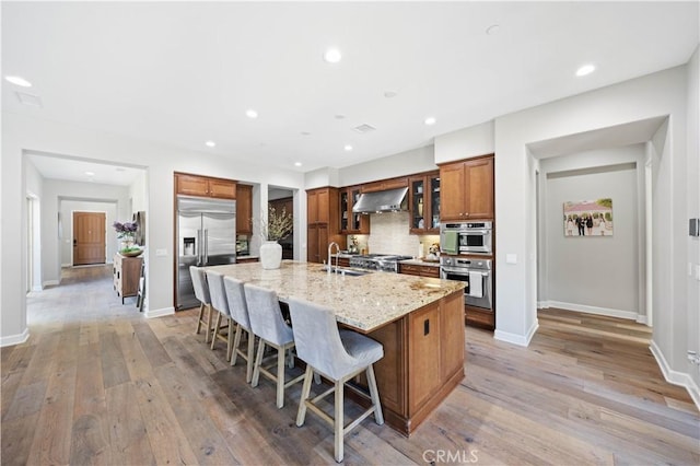 kitchen featuring a kitchen bar, a sink, range hood, appliances with stainless steel finishes, and brown cabinetry