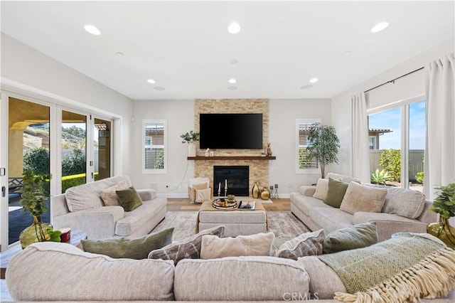 living area with recessed lighting, baseboards, a stone fireplace, and light wood-style flooring