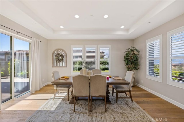 dining area featuring a tray ceiling, recessed lighting, baseboards, and light wood finished floors