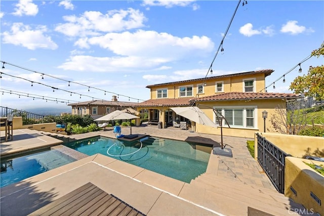 back of house with stucco siding, a patio, fence, and a pool with connected hot tub