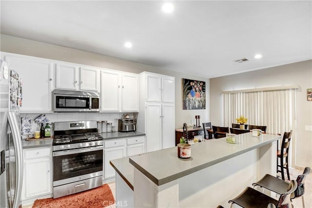 kitchen with visible vents, backsplash, a breakfast bar area, appliances with stainless steel finishes, and white cabinets