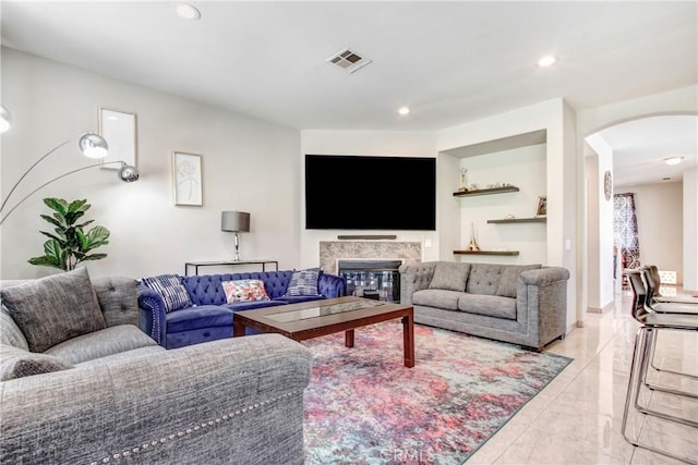 living area with visible vents, recessed lighting, arched walkways, a glass covered fireplace, and marble finish floor