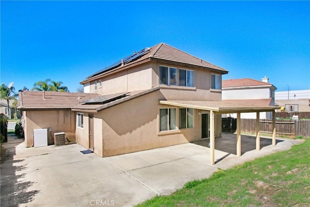 rear view of property with solar panels, a patio, fence, and stucco siding