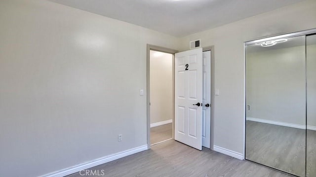 unfurnished bedroom with a closet, visible vents, baseboards, and wood finished floors