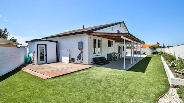 rear view of property with entry steps, a wooden deck, stucco siding, a lawn, and a fenced backyard