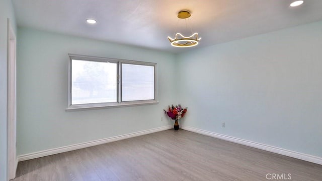 empty room with an inviting chandelier, recessed lighting, wood finished floors, and baseboards