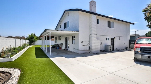 back of house with stucco siding, fence, a yard, cooling unit, and a chimney