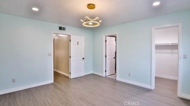 unfurnished bedroom with a spacious closet, visible vents, baseboards, and wood finished floors