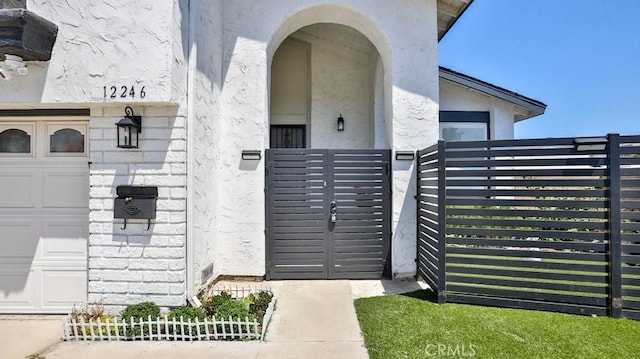 property entrance with stucco siding, fence, a garage, and a gate