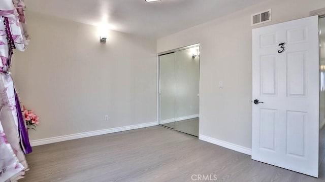 unfurnished bedroom with wood finished floors, visible vents, a closet, and baseboards