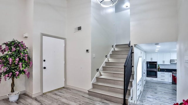 stairway with wood finished floors, visible vents, a towering ceiling, and baseboards