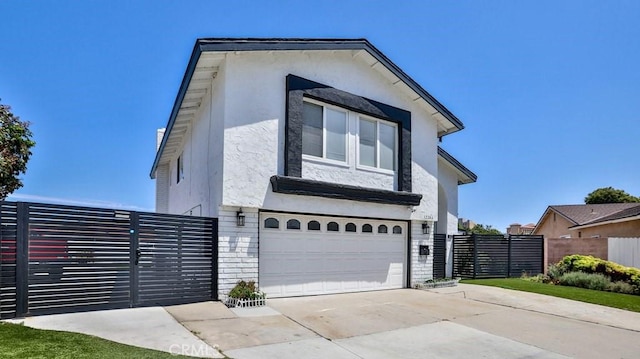 view of front of house with stucco siding, a gate, fence, concrete driveway, and a garage