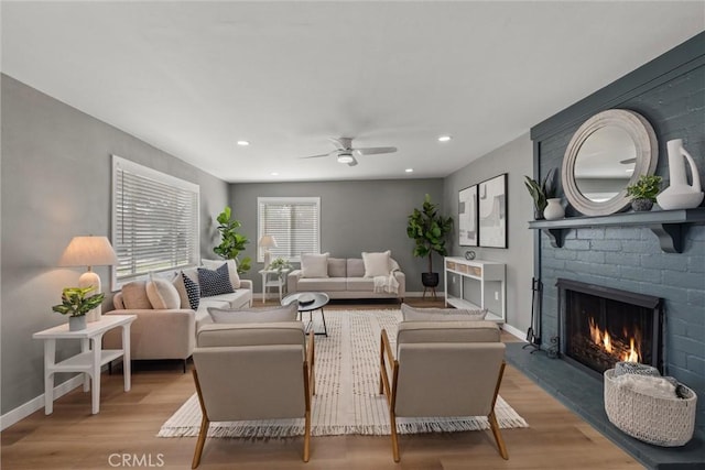 living area featuring a ceiling fan, wood finished floors, baseboards, recessed lighting, and a brick fireplace